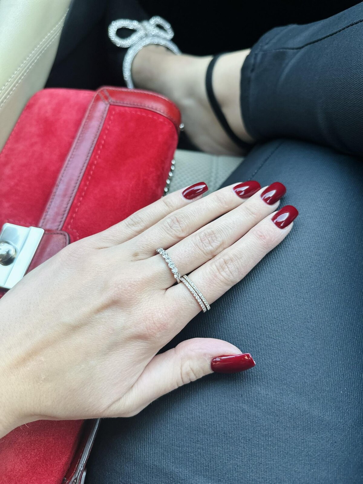 Engagement ring on hand in a car with red nails