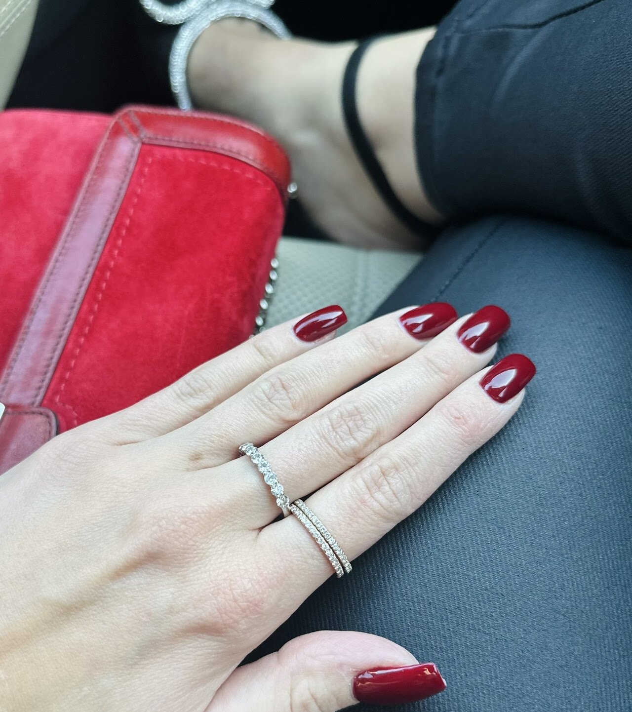 Hand wearing rings beside a red bag