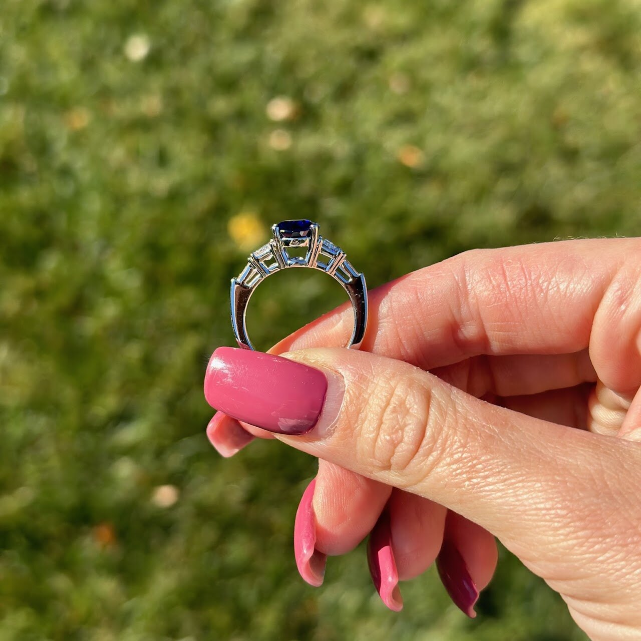 Engagement ring held outdoors against green grass